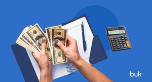 Mãos segurando notas de dinheiro ao lado de caderno e calculadora sobre fundo azul, representando o cálculo de salário líquido e o planejamento financeiro.